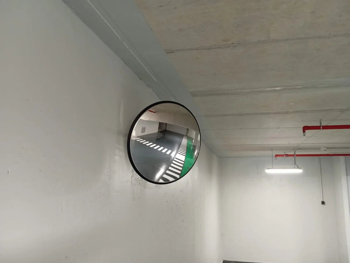 Specchio convesso fissato a una parete e rivolto verso la corsia di un parcheggio coperto.